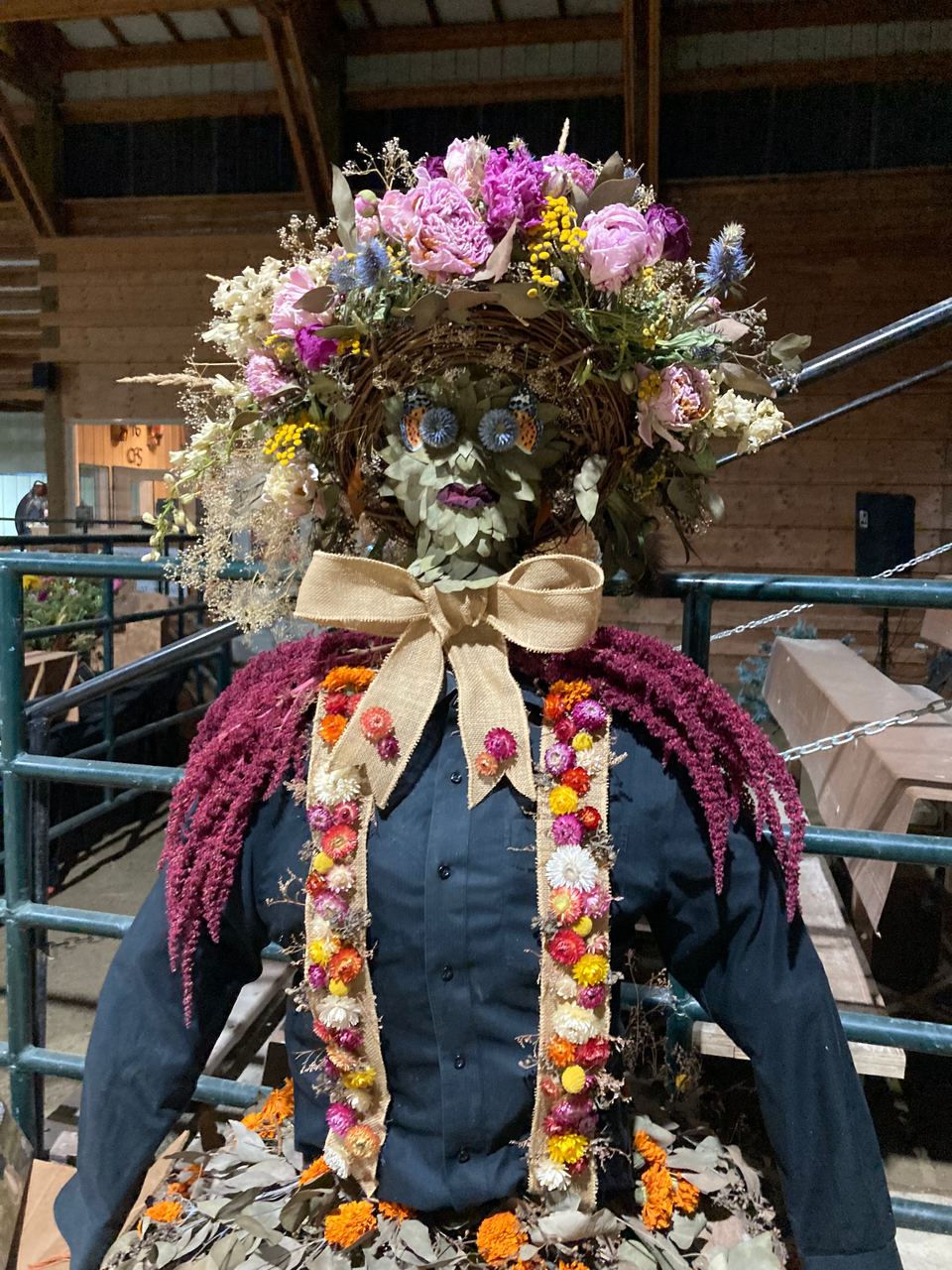 A scarecrow dressed in denim, crowned with dried flowers.