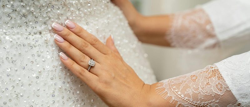 Close-up of hands resting on a beaded wedding gown with a lace sleeve