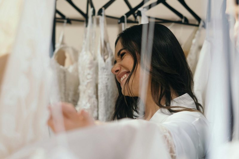 A smiling woman running her hand along a rail of wedding gowns