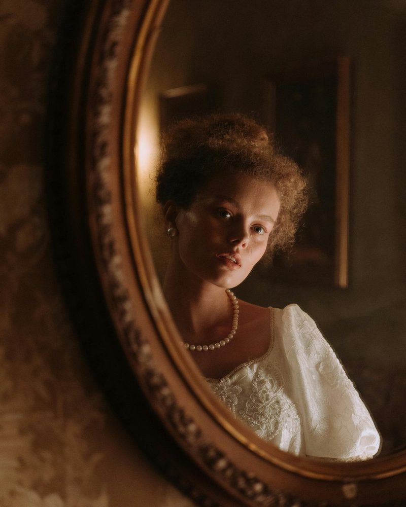 A bride in pearls reflected in an antique oval mirror