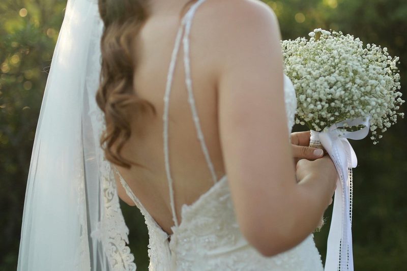 The back of a bride in a lace gown and veil holding baby's breath